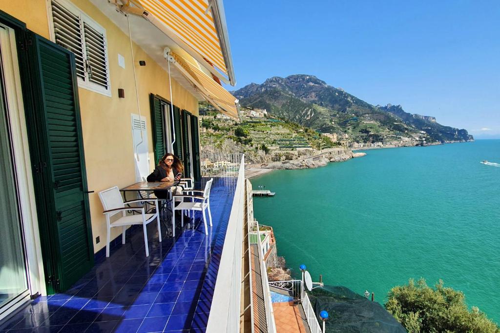 una donna seduta a un tavolo su un balcone con vista sull'oceano di Nel blu dipinto di blu a Ravello