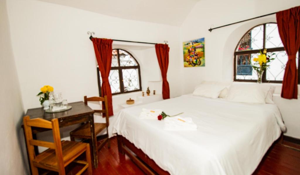 a bedroom with a white bed and a table with a chair at Posada Catama INN in Cusco