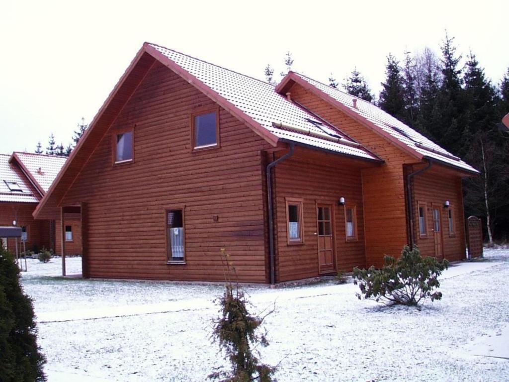 une grande maison en bois avec de la neige au sol dans l'établissement Ferienhaus Nr 24, Typ A, Ferienanlage Blauvogel, Hasselfelde, Harz, à Hasselfelde