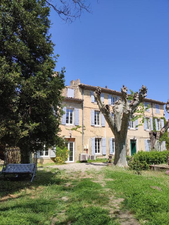 un grand bâtiment avec un arbre devant dans l'établissement Le mas Roc'amour, à Roquemaure