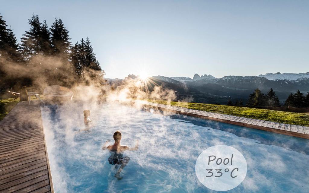 2 personas nadando en una piscina termal con vapor en Granpanorama Wellnesshotel Sambergerhof Superior, en Villandro