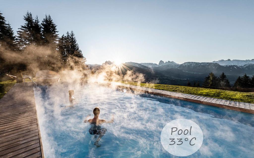 zwei Personen schwimmen in einem Thermalbecken mit Dampf in der Unterkunft Granpanorama Wellnesshotel Sambergerhof Superior in Villanders