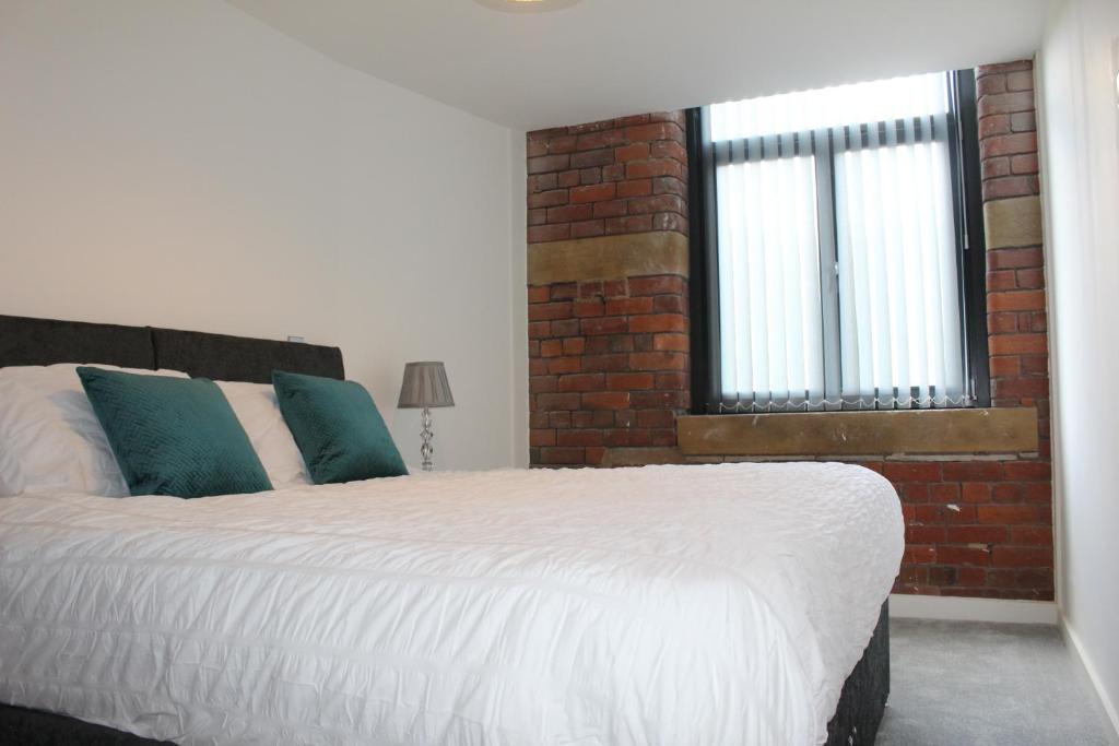 a bedroom with a white bed with a brick wall at Luxury Serviced Apartments in Bradford