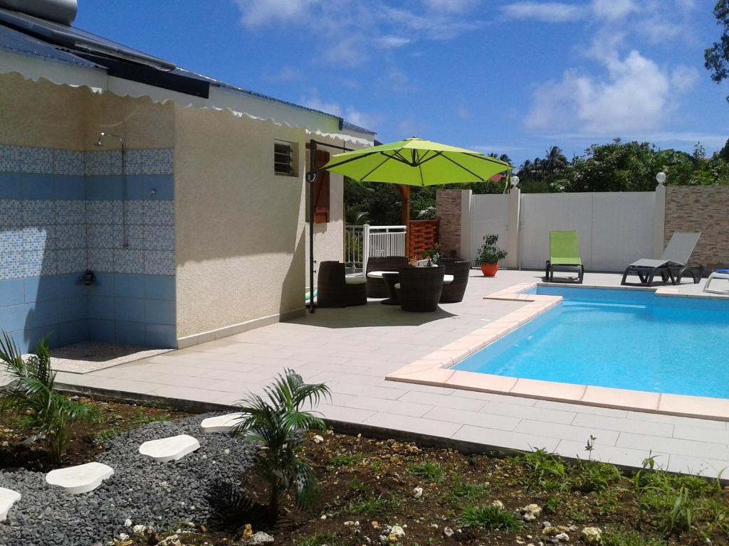 a swimming pool with a green umbrella next to a house at Aux petits flots in Le Gosier