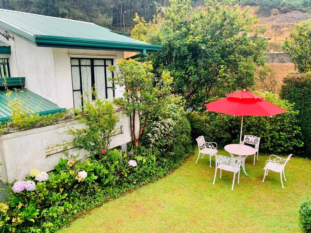 a table and chairs with a red umbrella in a yard at Miliya Guest House in Nuwara Eliya