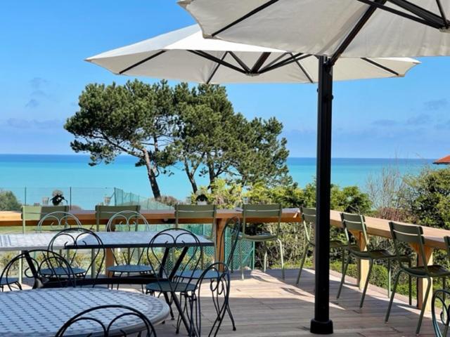 a patio with tables and chairs and an umbrella at Hôtel De La Terrasse in Varengeville-sur-Mer