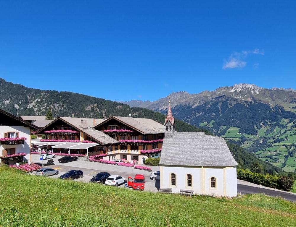 a building with a church and a parking lot with cars at Sporthotel Kalcherhof in Racines