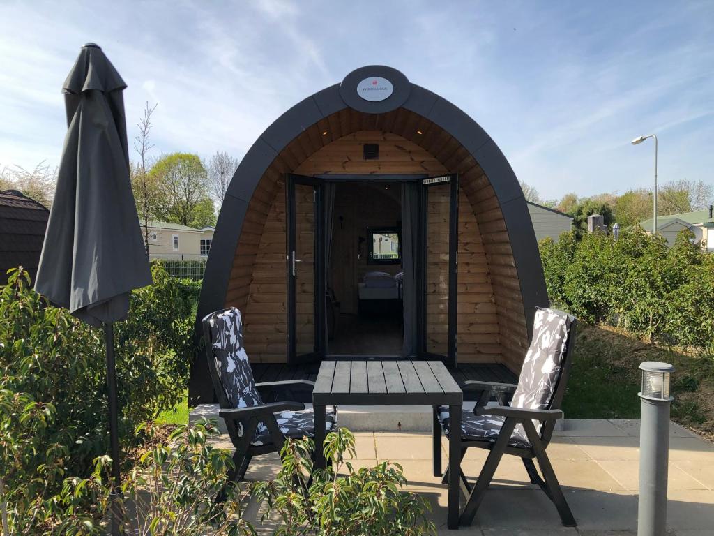 un refugio de madera con 2 sillas, una mesa y una sombrilla en Woodlodge High Chaparral en Oirsbeek