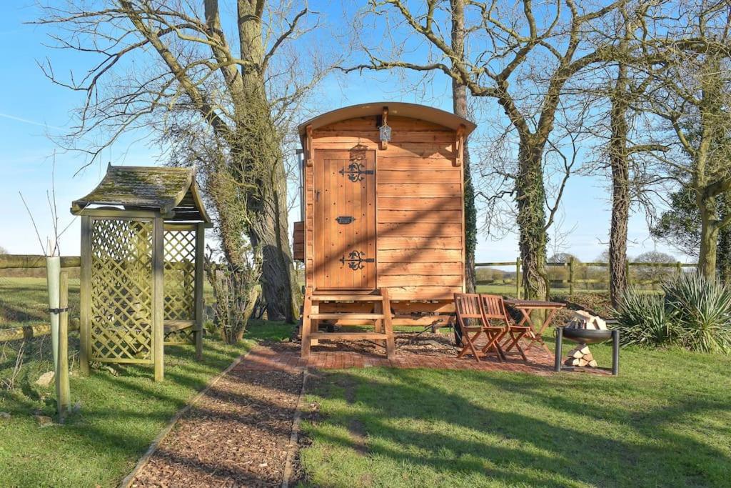 a wooden out house with a bench in the grass at Handcrafted Shepherds Hut in Toppesfield