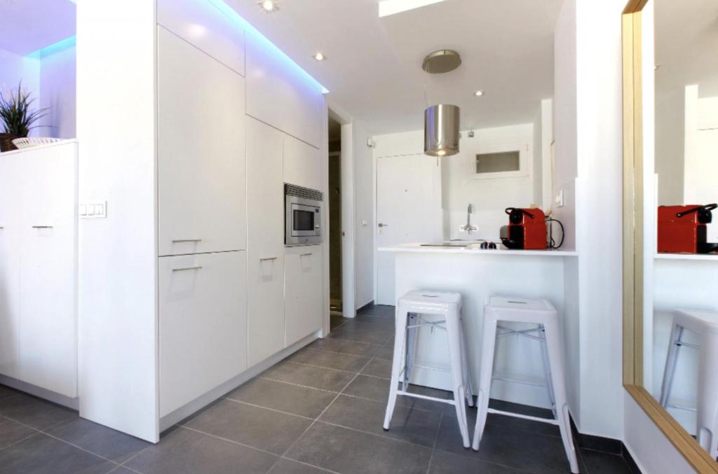 kuchnia z białymi szafkami i stołkami w obiekcie Precioso apartamento con vistas al mar y piscinas w mieście Benalmádena