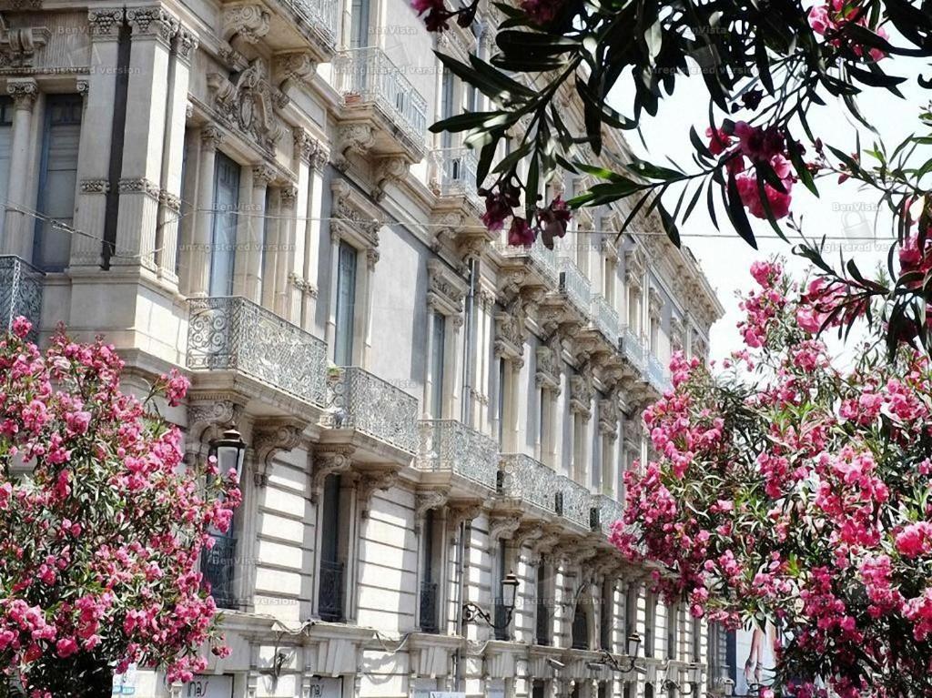 un grand bâtiment avec des fleurs roses devant lui dans l'établissement B&B Elios Rooms, à Catane