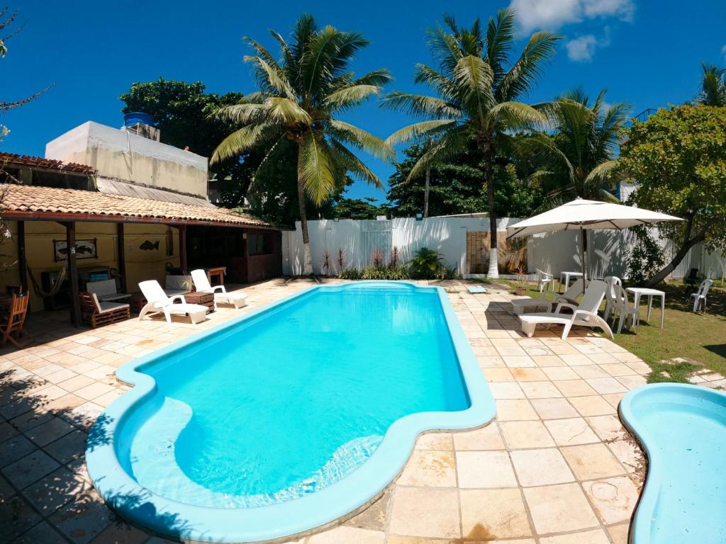 a swimming pool in a yard with chairs and an umbrella at Pousada Parador 081 in Porto De Galinhas