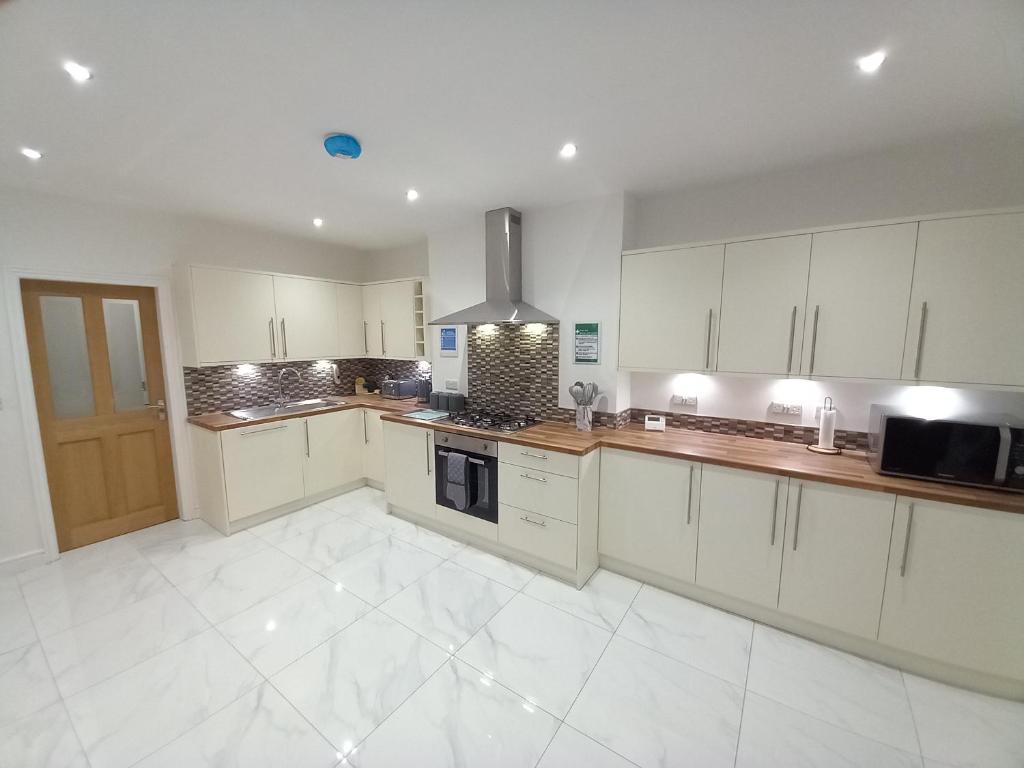 a large kitchen with white cabinets and a stove at Spacious & Modern 4 Bedroom Holiday Home Gwynedd in Bangor