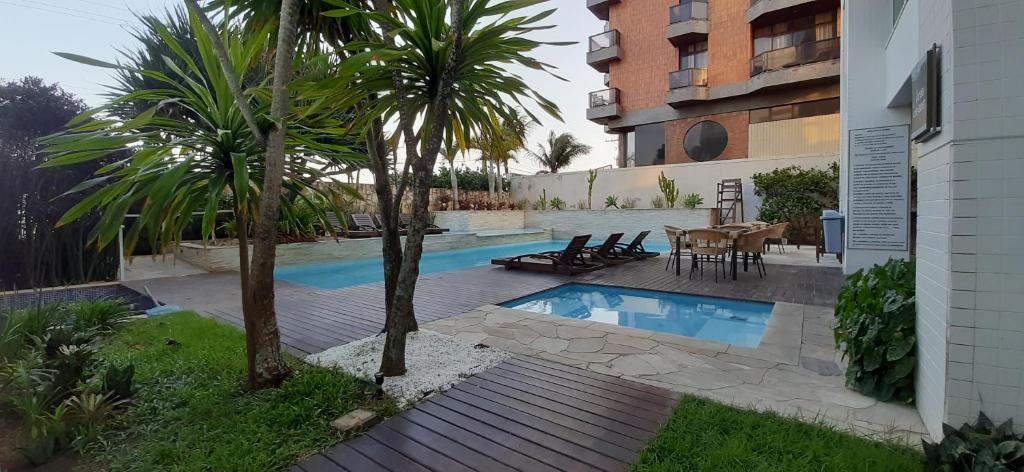 a swimming pool with a table and two palm trees at Flat 404 Hotel Mandai in Cabo Frio