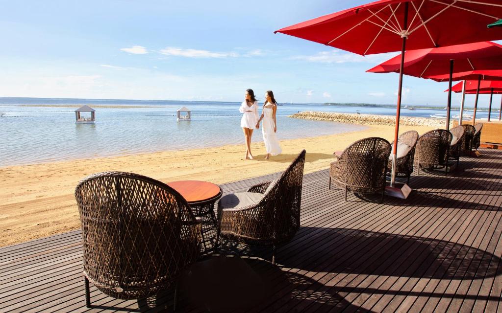 a beach area with chairs, tables and umbrellas at Puri Santrian in Sanur
