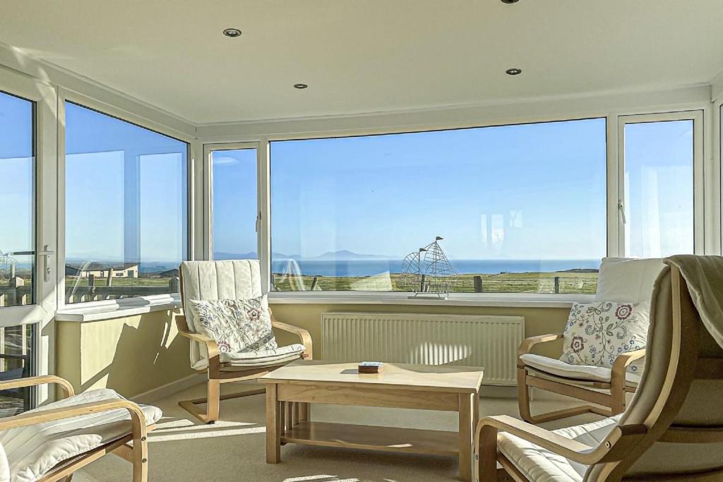 a living room with chairs and a table and windows at Plas Diwedd in Valley