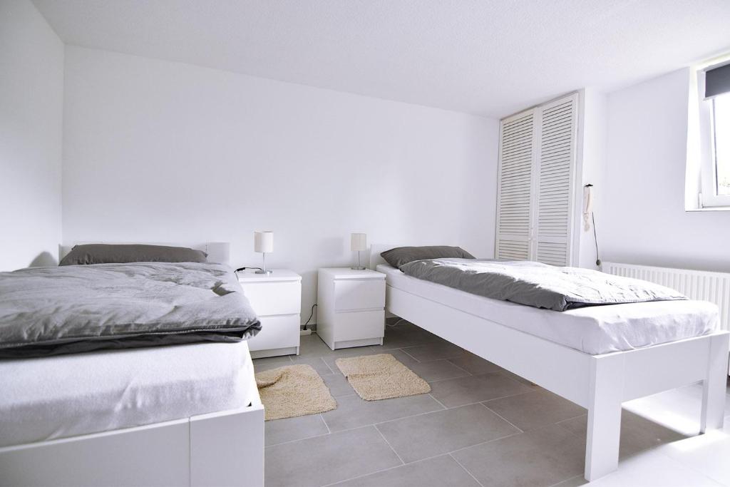 a white bedroom with two beds and a window at Souterrain apartment in Wesseling in Wesseling