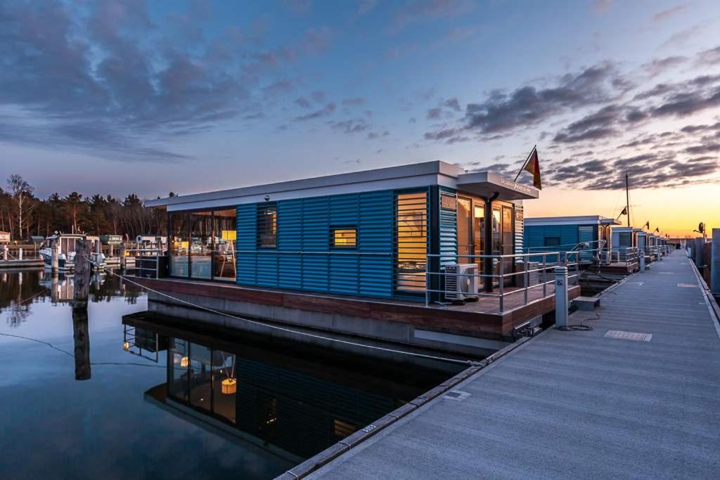 ein blaues Gebäude auf einem Dock neben dem Wasser in der Unterkunft Floatinghouses Peenemünde in Peenemünde