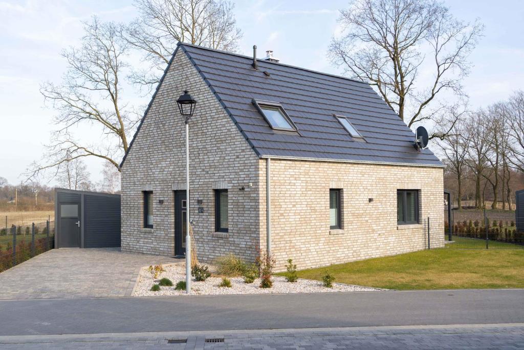 a small brick house with a black roof at Ferienhaus Seeblick am Harkebrügger See mit Sauna und Kamin in Barßel