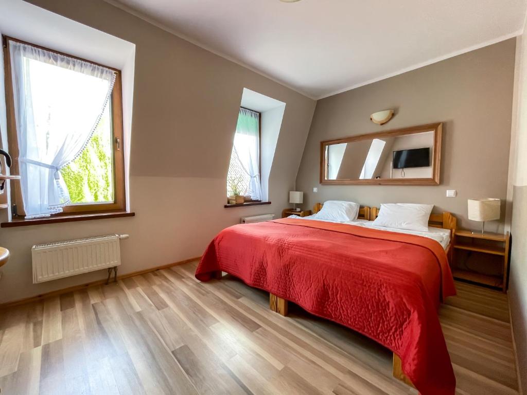 a bedroom with a red bed and two windows at Aparthotel Mikołajki in Mikołajki