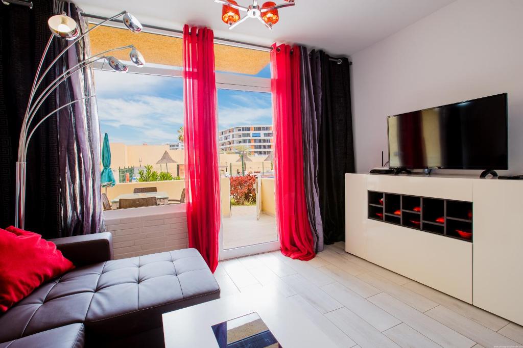 ein Wohnzimmer mit roten Vorhängen und einem großen Fenster in der Unterkunft Bungalow Costa Adeje Cortijo 1-8 in Playa de las Americas