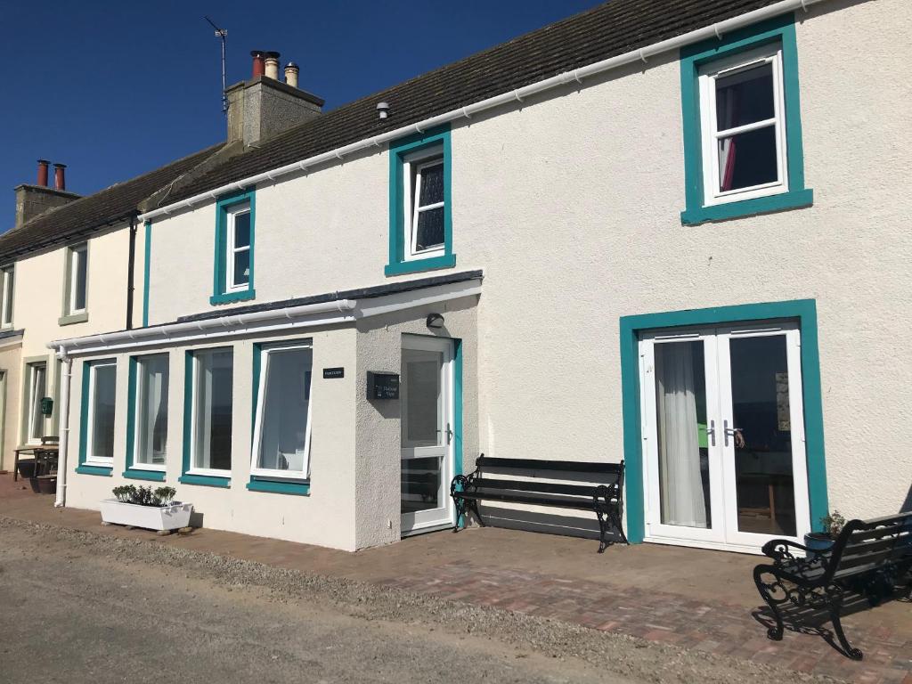 a white building with blue windows and a bench at Lovely 3-Bed Cottage Portmahomack next to harbour in Portmahomack