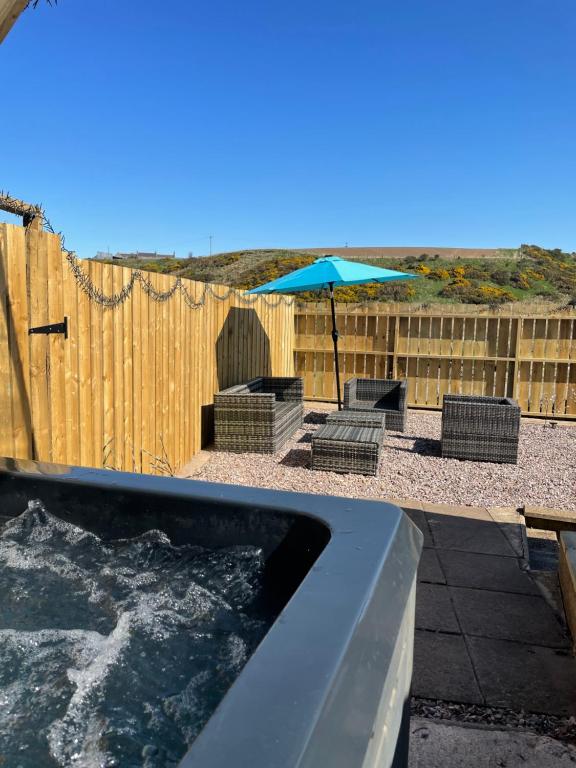 a hot tub with chairs and an umbrella next to a fence at The Steading with 7 Seater Hot Tub Aberdeenshire in Banff