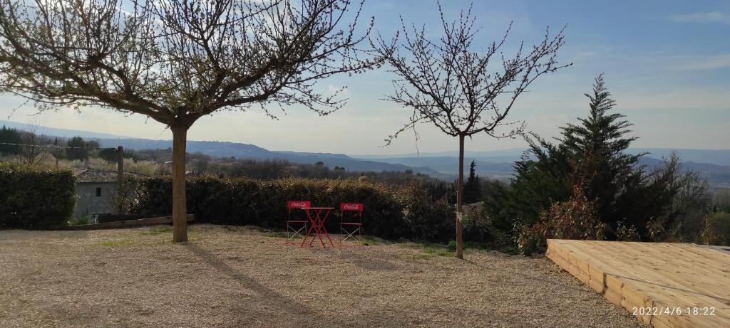 twee rode stoelen en een tafel onder een boom bij Une escapade en Luberon in Bonnieux