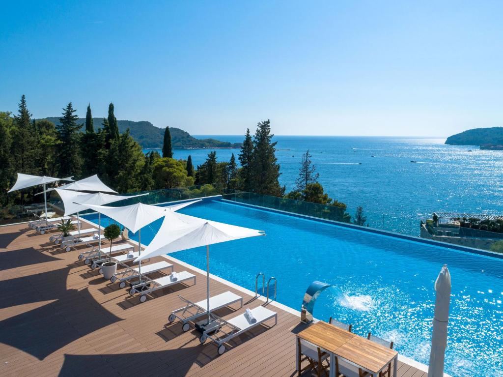 a swimming pool with chairs and umbrellas and the ocean at Dukley Hotel & Resort in Budva