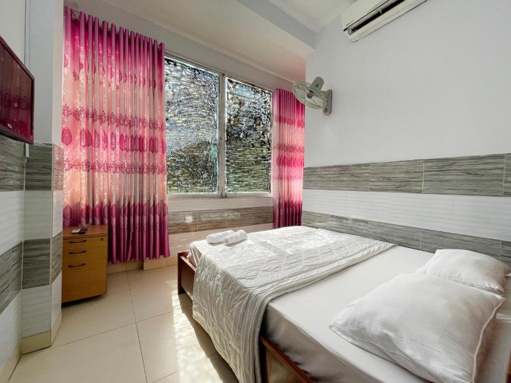 a bedroom with a bed and a window with pink curtains at Huy Hoàng Hotel in Ho Chi Minh City