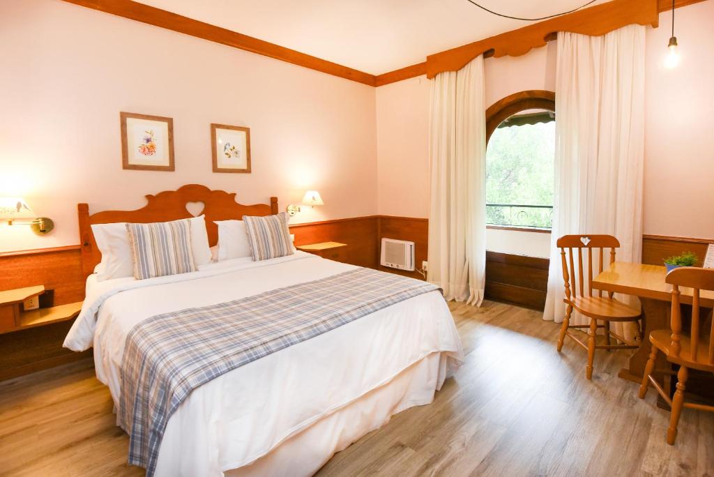 um quarto com uma cama, uma mesa e uma janela em Hotel das Hortênsias em Gramado