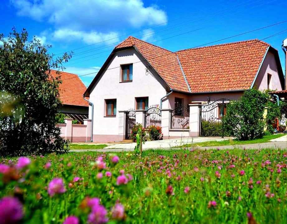 una casa blanca con techo rojo y un campo de flores en Rózsalugas Vendégház, en Szilvásvárad