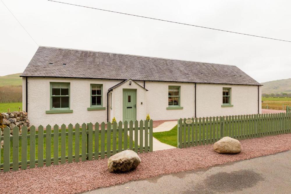 a white house with a fence and two rocks at Balbeg Cottage in Straiton