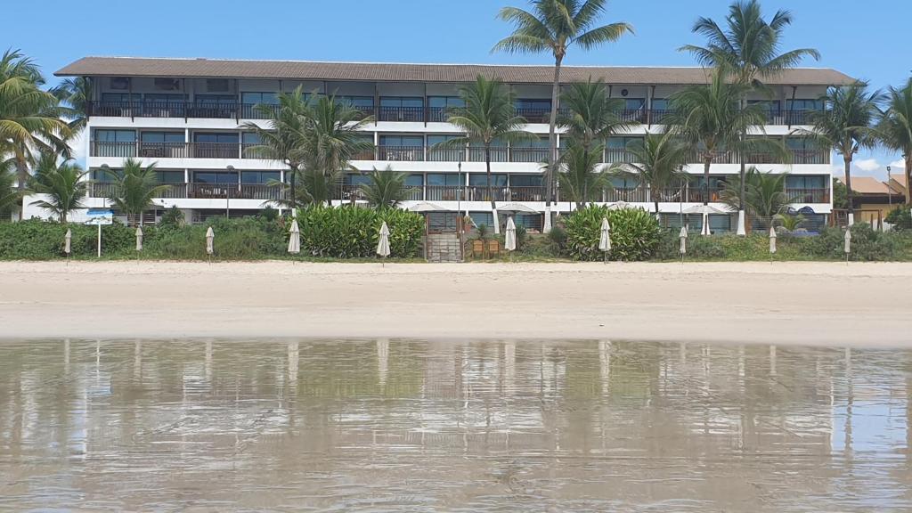 ein Gebäude mit Palmen vor einem Wasserkörper in der Unterkunft Porto Beach Flat in Porto De Galinhas