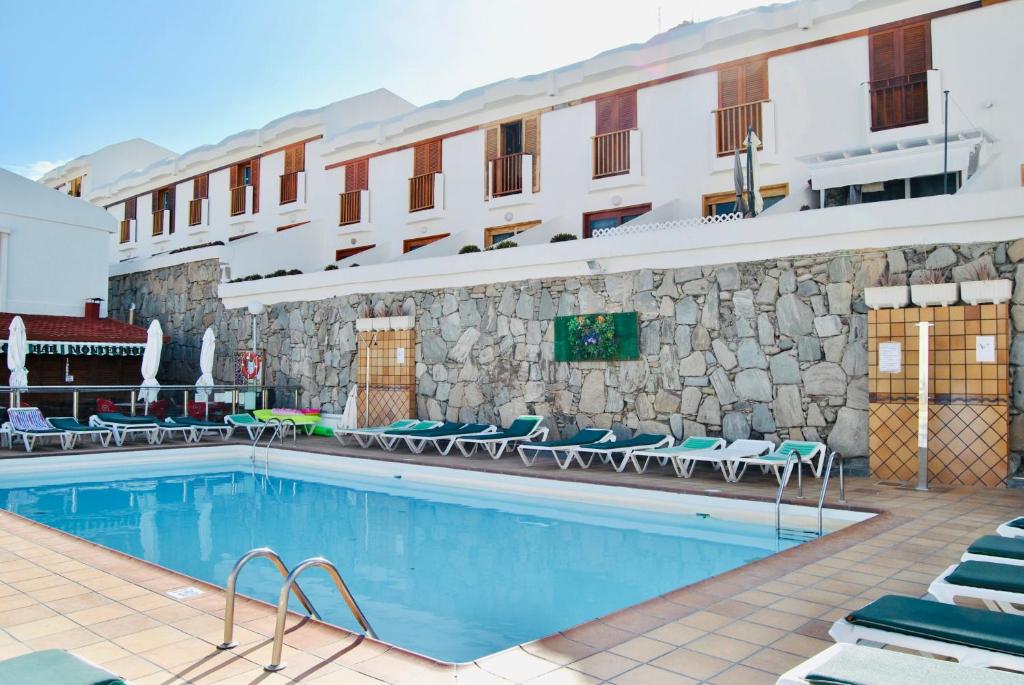a hotel swimming pool with chairs and a building at Bungalow montecarlo 35 and 45 first row with air conditioning&WI-FI and sound insulation in Puerto Rico de Gran Canaria