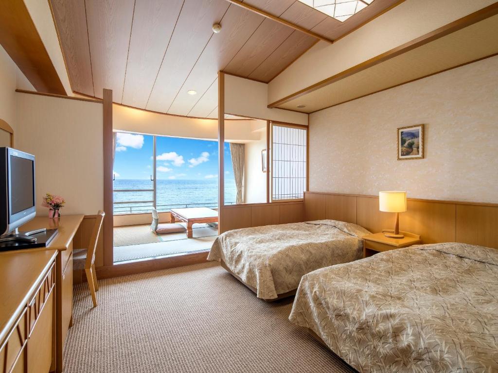 a bedroom with two beds and a television and a balcony at Mikazuki Sea-Park Hotel Katsuura in Katsuura
