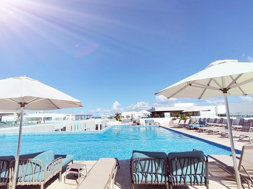 una piscina con sillas y sombrillas en IPANA Luxury Apartments by Vacaciones.Yeah en Playa del Carmen