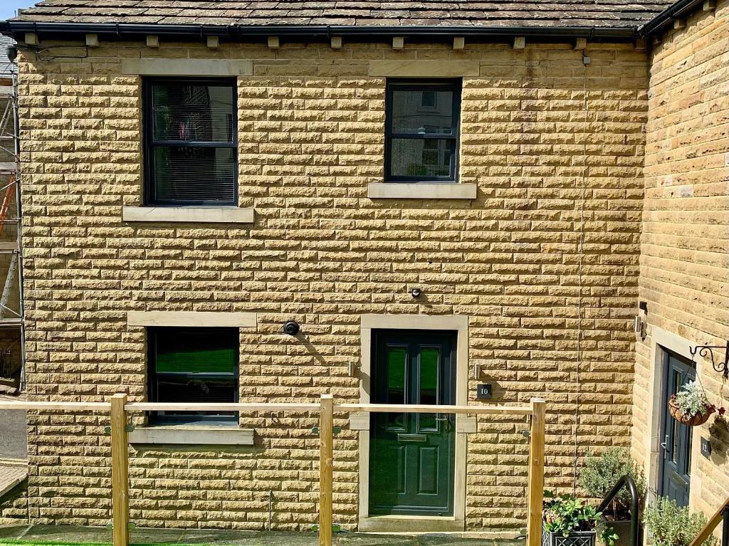 Un edificio de ladrillo con una puerta y ventanas verdes. en Victoria House, en Holmfirth