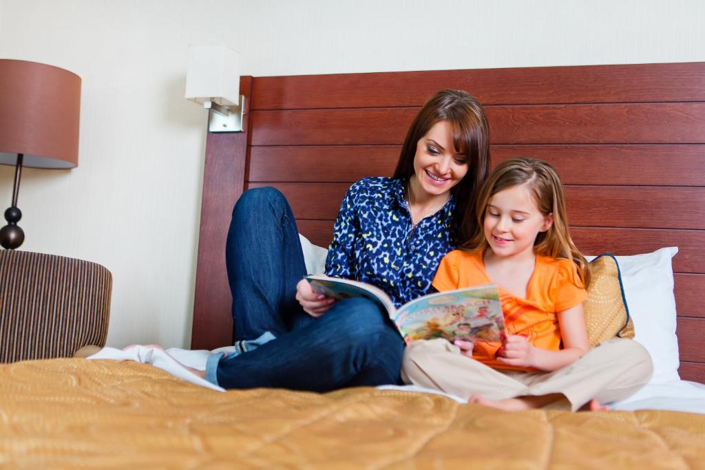 a woman and a girl sitting on a bed reading a book at West Edmonton Mall Inn in Edmonton