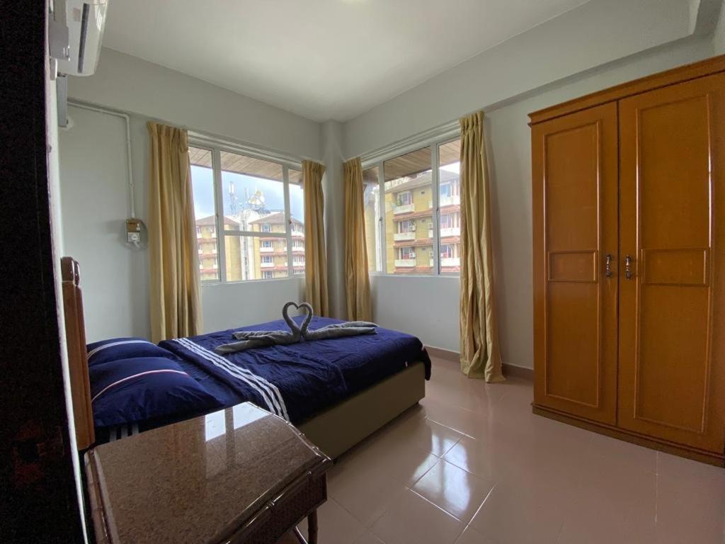 a bedroom with a bed and a table and windows at D’lina pelangi in Kemaman