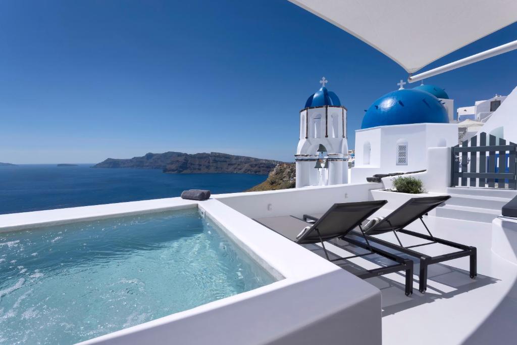 a plunge pool on the roof of a house with chairs and a lighthouse at Bluedome Cavehouses Santorini in Oia