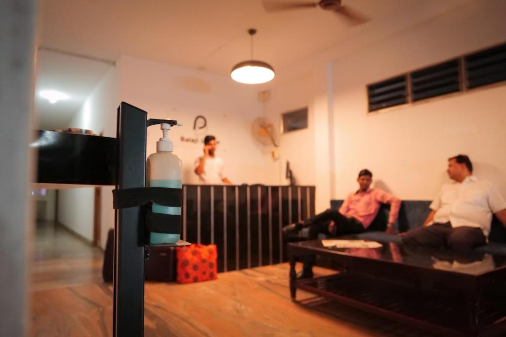 three men sitting on a couch in a living room at Balaji Lodge in Villupuram