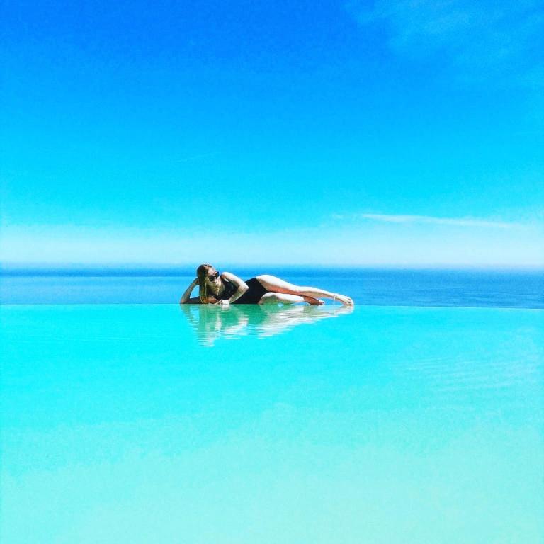 a woman laying on a surfboard in the water at Hotel Antica Cascina Del Golfo in Scopello