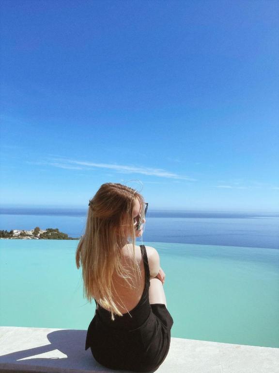 a woman sitting next to a pool looking out at the water at Hotel Antica Cascina Del Golfo in Scopello