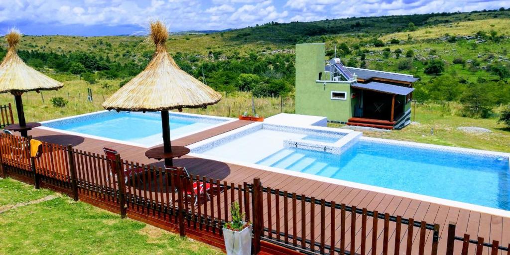 a swimming pool with two umbrellas on a fence at Cabañas Mirador del Valle Villa Giardino in Córdoba