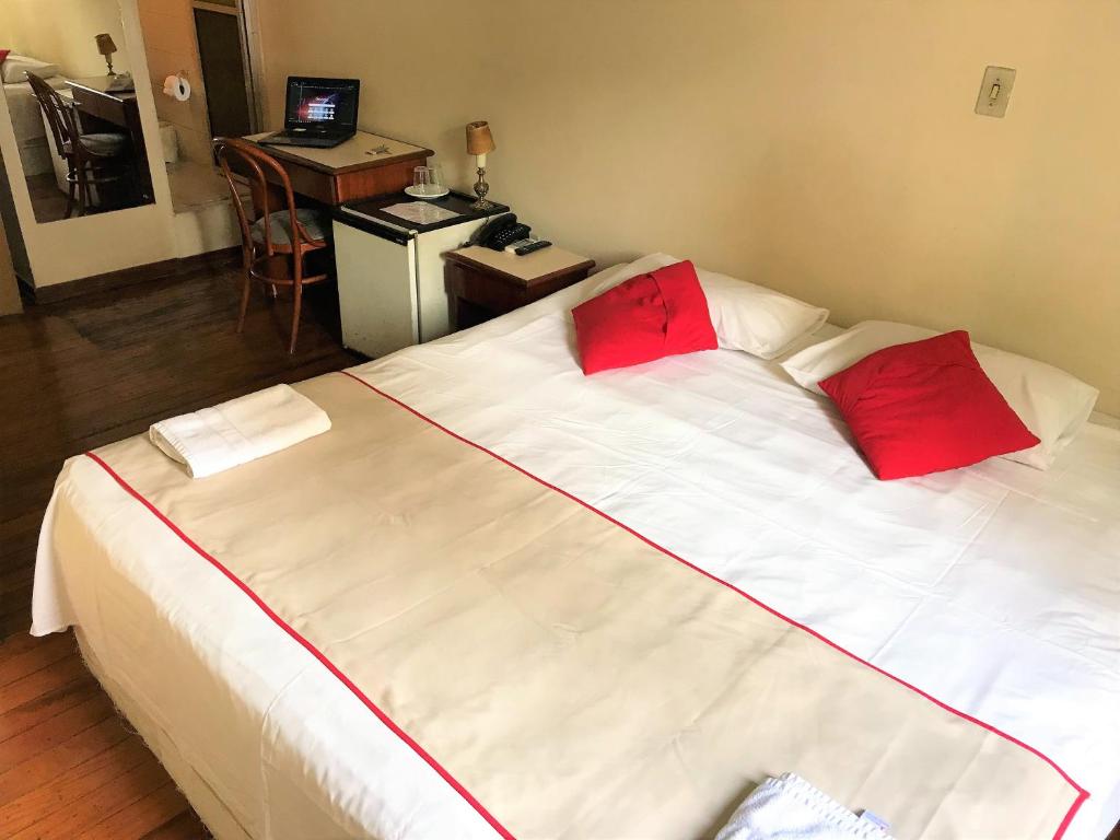 uma grande cama branca com almofadas vermelhas num quarto em Hotel São Jorge São Paulo - By UP Hotel - próximo a 25 de março, fácil acesso ao Expo Center Norte e Mercado Municipal SP em São Paulo