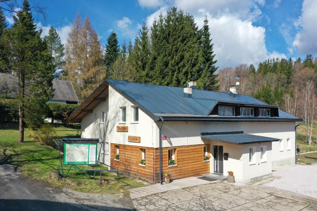 a white house with a black roof with a sign in front at Pension Lesná in Jiřetín pod Jedlovou