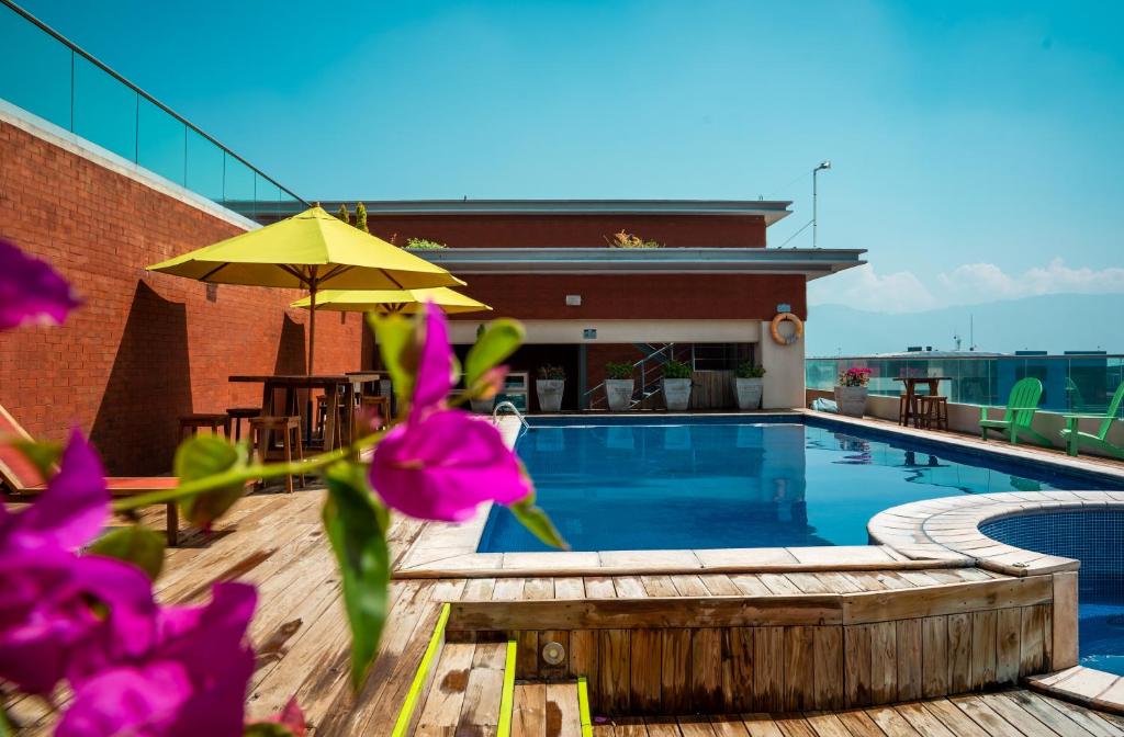 uma piscina com um guarda-chuva amarelo e flores roxas em LATAM HOTEL Plaza Pradera Quetzaltenango em Quetzaltenango