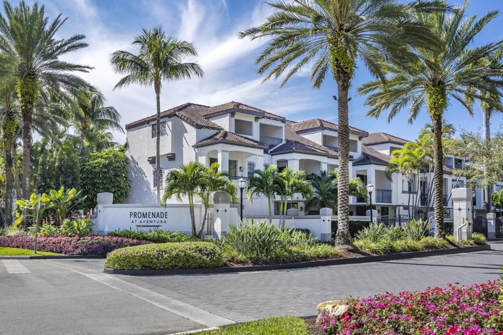 een groot wit gebouw met palmbomen en bloemen bij Modern Townhouse Apartments near the Turnberry Golf Course, Aventura Mall, and Sunny Isles Beach in Aventura