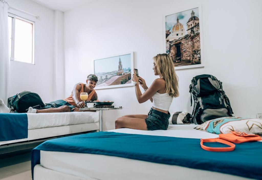 una mujer sentada en una cama tomando una foto de un hombre en Neos Hotel Cartagena, en Cartagena de Indias